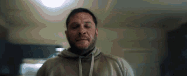 a man with a beard wearing a hoodie is standing in a room .