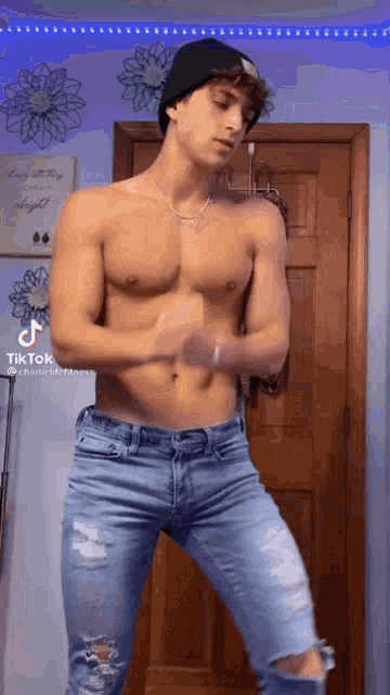 a shirtless young man in ripped jeans and a beanie is dancing in a room .