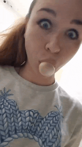a woman is blowing a bubble in her mouth while wearing a sweater .