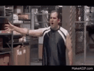 a man in a black and white tank top is standing in a warehouse with his arms outstretched .