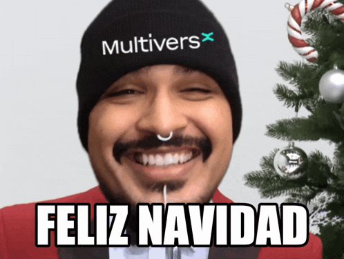 a man wearing a beanie that says multivers on it smiles in front of a christmas tree