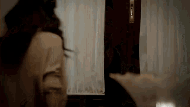 a woman is standing in front of a door in a room with white curtains .