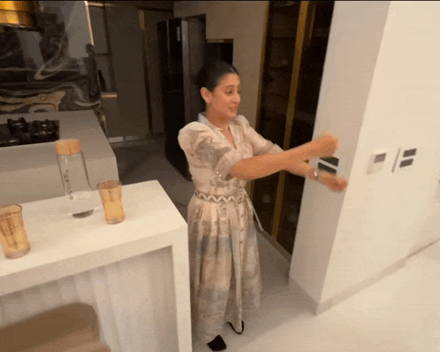 a woman in a dress is standing in a kitchen with a bottle of water on the counter
