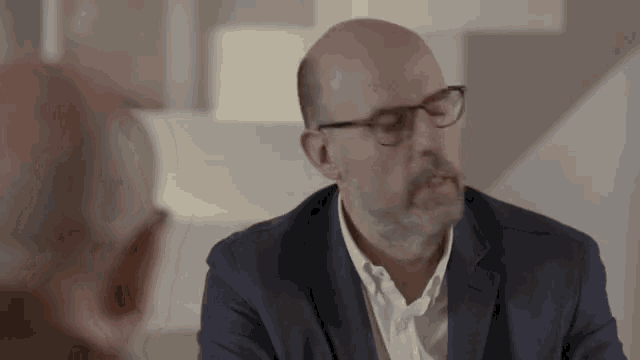 a man wearing glasses and a suit is talking to another man