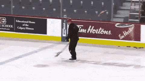a hockey player is sweeping the ice with a broom in front of a tim hortons ad