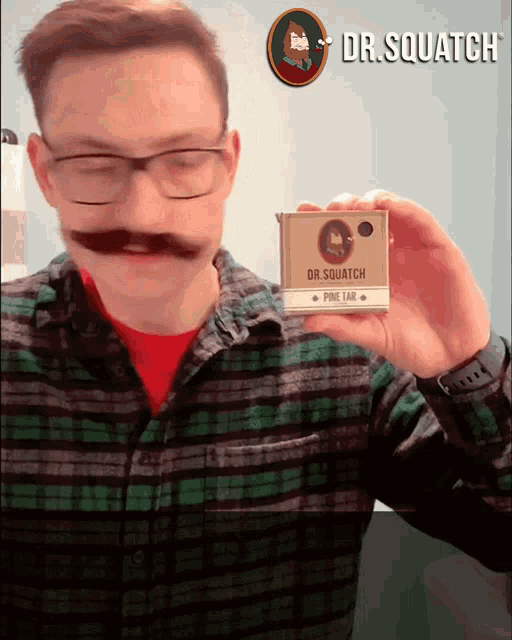 a man with a fake mustache is holding a dr.squatch pine tab
