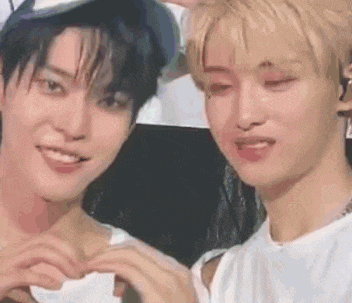 two young men are making a heart shape with their hands and smiling .