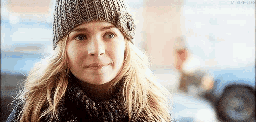 a woman wearing a knitted hat and scarf smiles