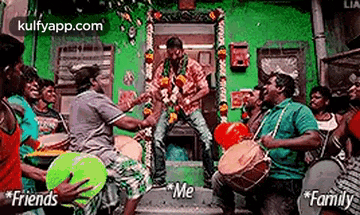 a group of men are playing drums in front of a green building and a man is standing in the middle of the group .