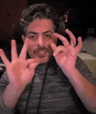 a man with a mustache and a ring on his finger is making a funny face with his hands .