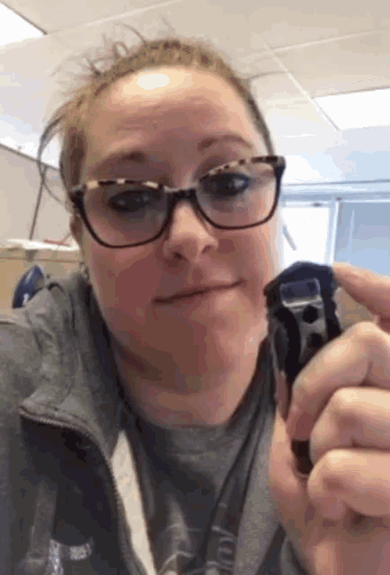 a woman wearing glasses and a grey shirt is holding something in her hand