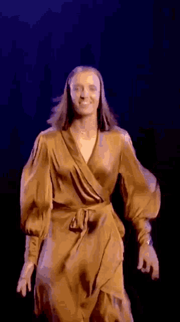 a woman is wearing a gold wrap dress and smiling .