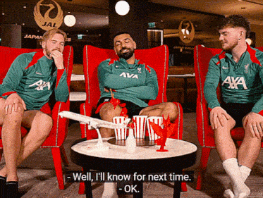 a man in a green aya shirt sits with two other men