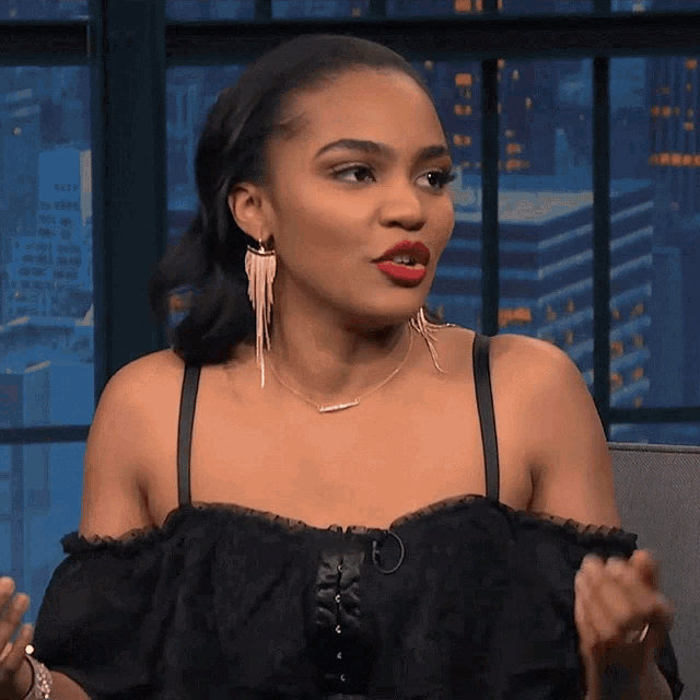 a woman wearing a black off the shoulder top and earrings is sitting on a couch