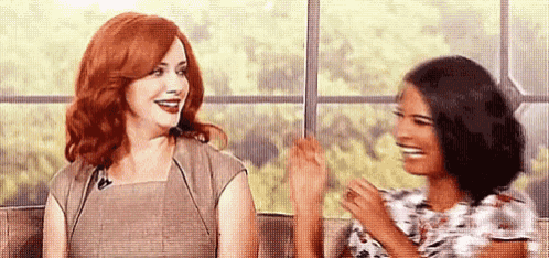 two women are sitting next to each other in front of a window .