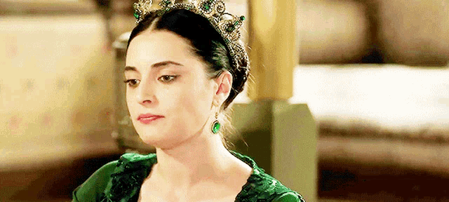 a woman in a green dress and emerald earrings is wearing a crown on her head .