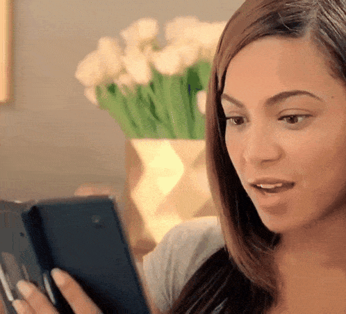 a woman looks at a cell phone with a vase of flowers in the background