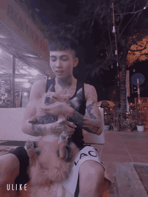 a tattooed man holds a small dog while wearing a black tank top and white shorts that say ac
