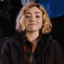 a woman with blonde hair wearing a brown jacket is smiling