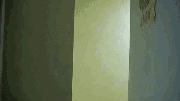 a person is standing in a hallway next to a wall with a hole in it .