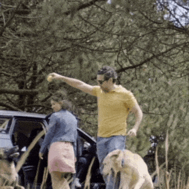a man in a yellow shirt is standing next to a dog in a field