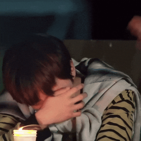 a person covering their face with their hand while holding a lit candle