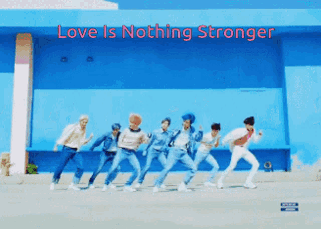a group of young men are dancing in front of a blue wall with the words love is nothing stronger