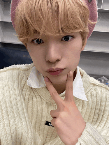 a young man wearing a white sweater and a pink hat is making a face