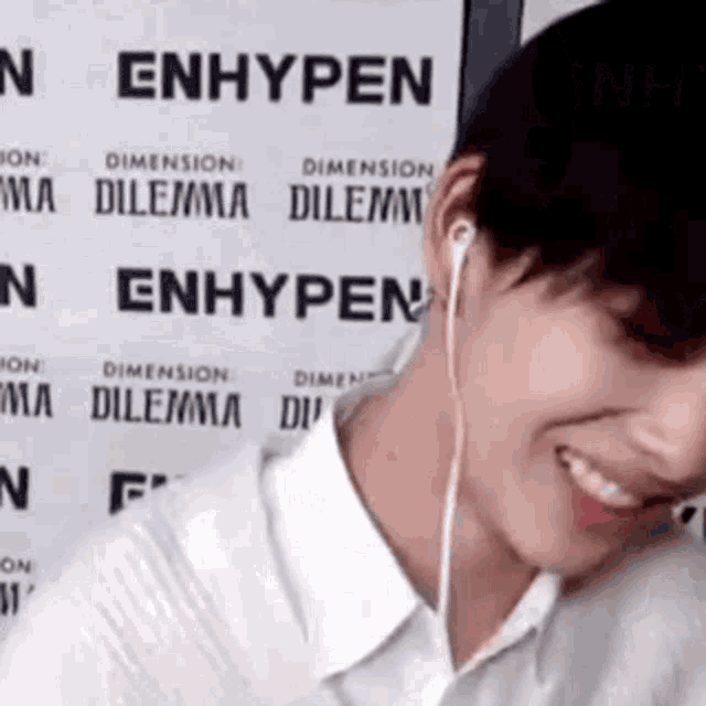 a man wearing headphones is smiling in front of a sign that says enhypen