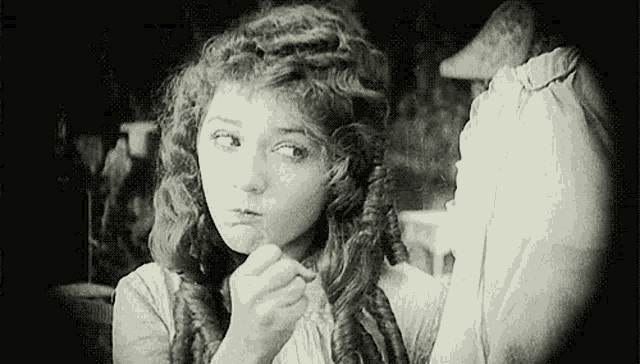 a black and white photo of a woman with curly hair looking at herself in a mirror .