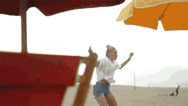 a woman is dancing on the beach with an orange umbrella