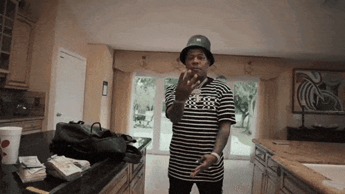 a man wearing a black hat and a black and white striped shirt is standing in the kitchen