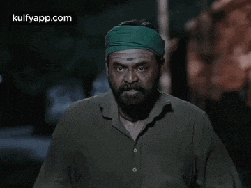 a man with a beard and a green headband is standing in the dark .