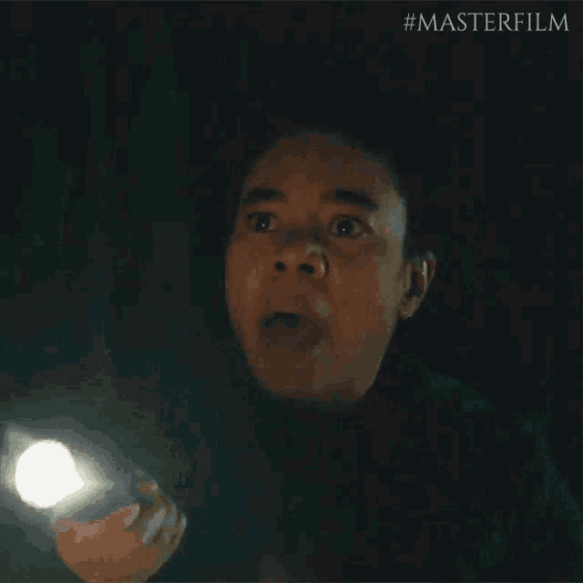 a woman is holding a flashlight in her hand in the dark and making a funny face .