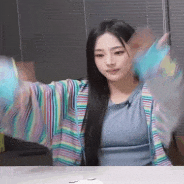 a woman is sitting at a table with her arms outstretched and wearing a colorful cardigan .