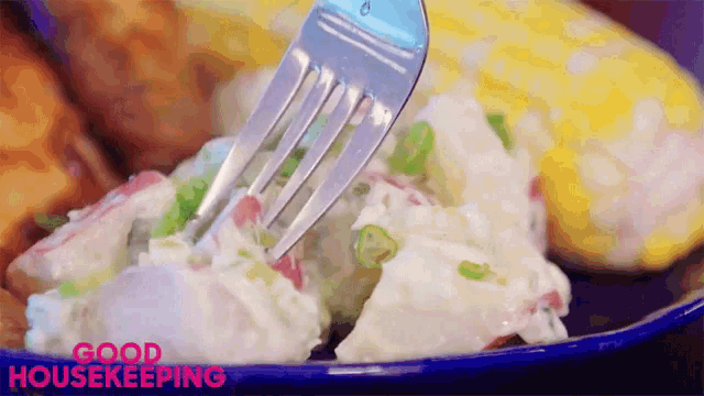 a close up of a fork taking a piece of potato salad