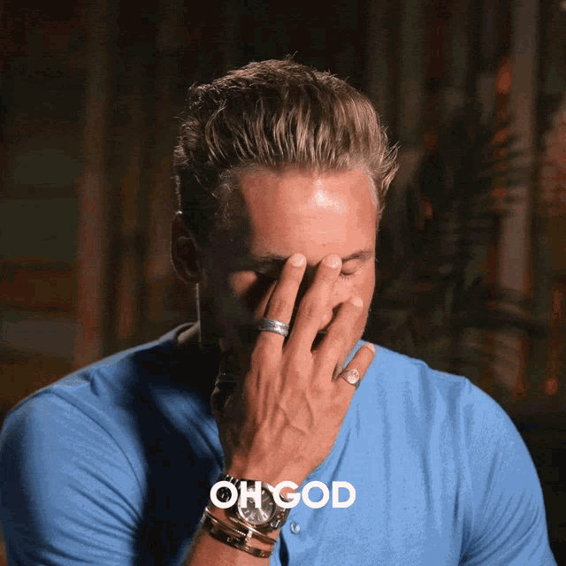 a man in a blue shirt is covering his face with his hand and the words oh god are visible behind him