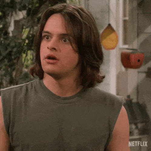 a man with long hair is wearing a green tank top and making a funny face .