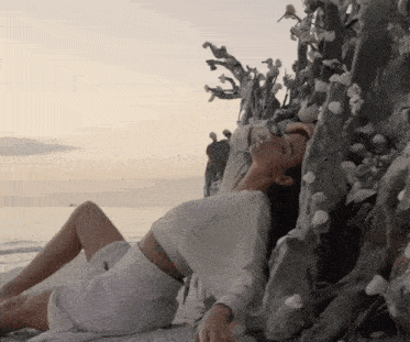 a woman laying on the beach with her head on a tree
