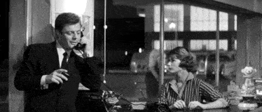 a man in a suit and tie talking on a phone next to a woman