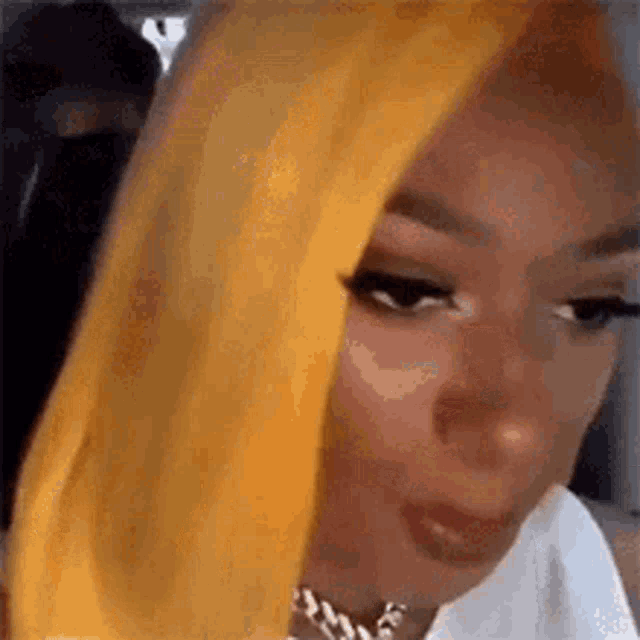 a woman with yellow hair is wearing a white shirt and a necklace .
