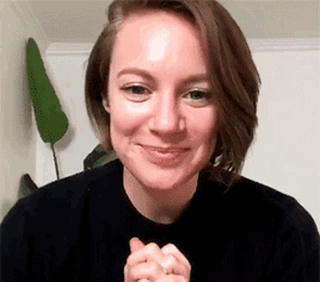 a woman in a black sweater is smiling with her hands folded .