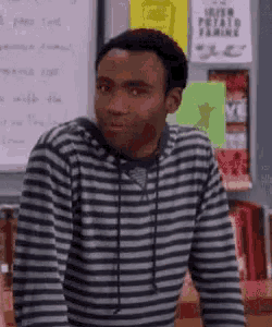 a man in a striped shirt is standing in front of a whiteboard .