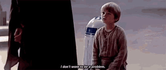 a little boy is kneeling down in front of a r2d2 robot and talking to a man .