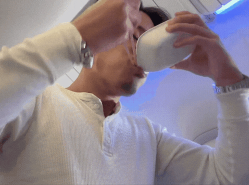 a man in a white shirt is drinking from a cup