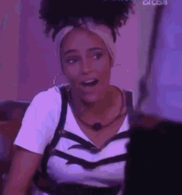 a woman wearing a headband and a white shirt is sitting on a couch with her mouth open .