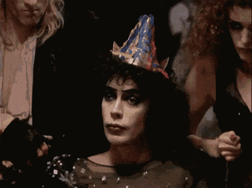a woman wearing a party hat is standing in a dark room with other people .