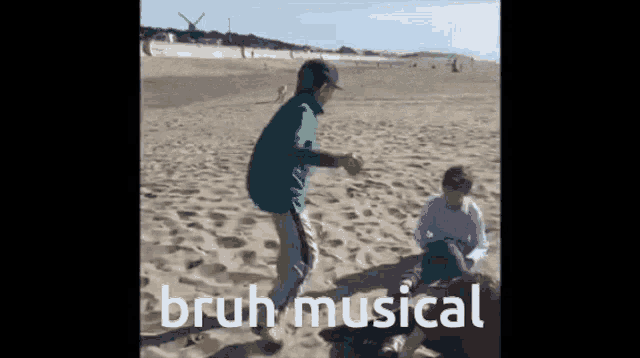 a man in a green shirt is dancing on a sandy beach while another man sits on the sand .