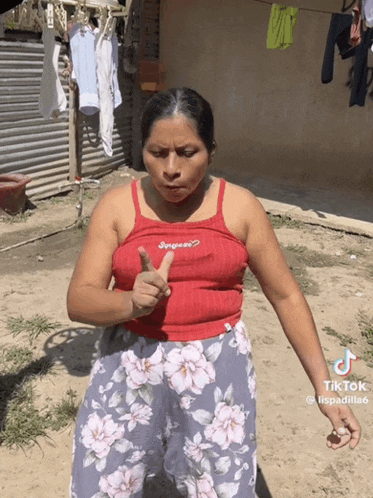 a woman in a red tank top and floral pants is giving a thumbs up sign
