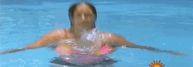 a woman in a bathing suit is splashing in a pool with a sun in the background